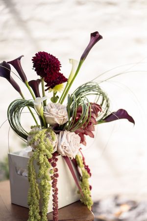 Elegant wedding floral arrangement featuring dark calla lilies, burgundy dahlias, and green amaranthus.