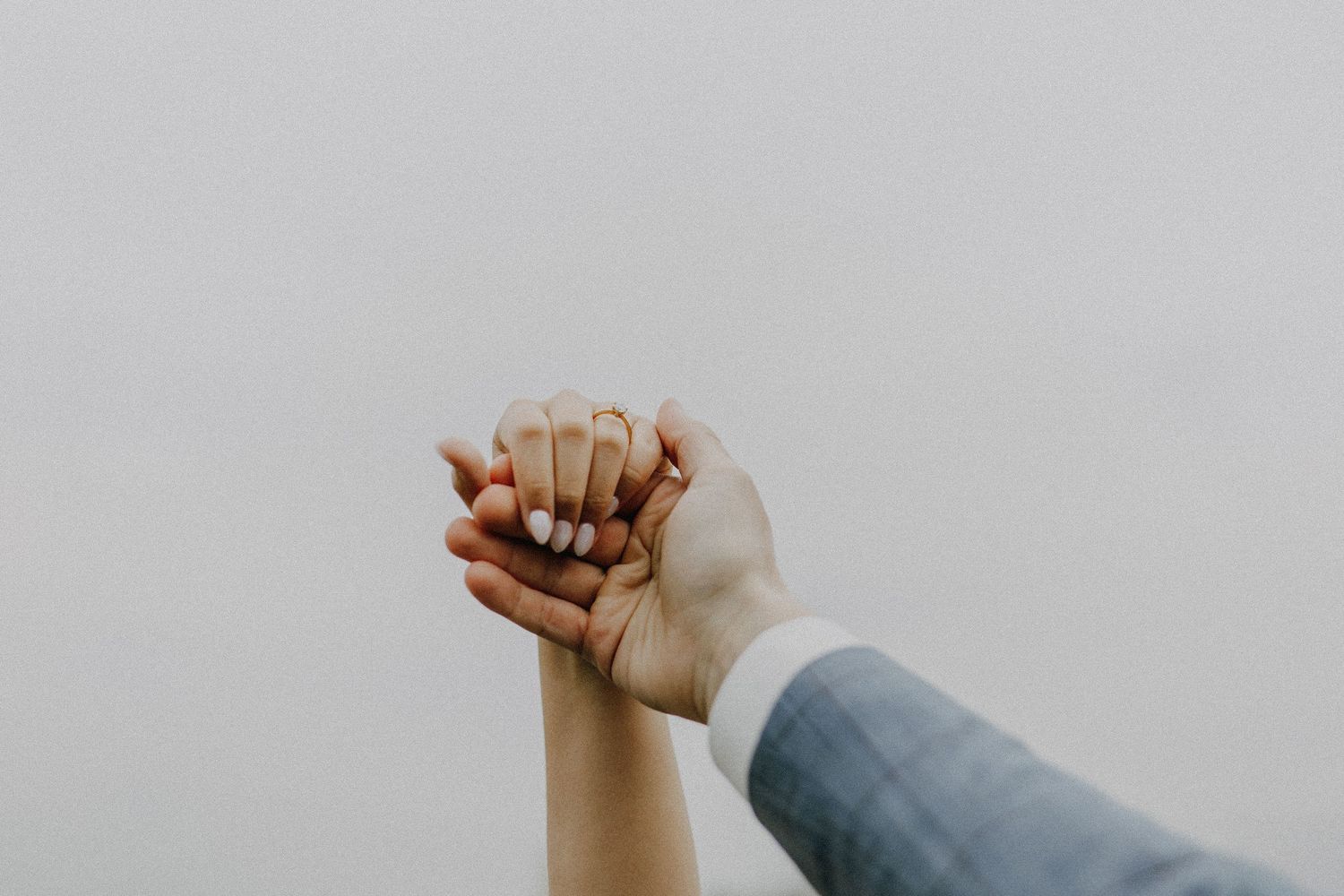 Two hands raised together against a gray sky, showing an engagement ring, symbolizing love and commitment.