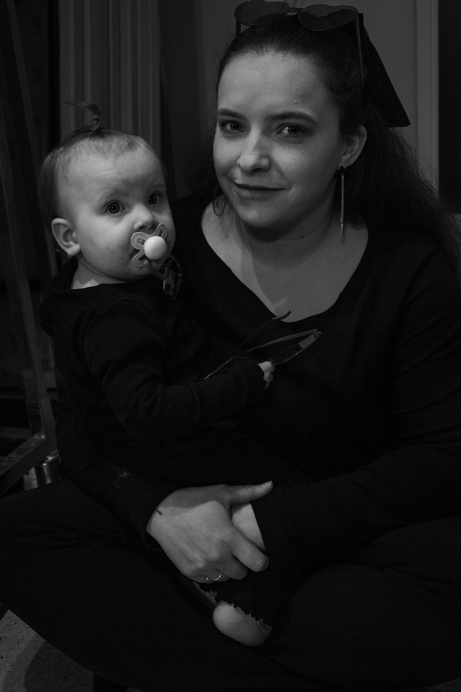Black and white portrait of a young woman holding a baby with a pacifier indoors.