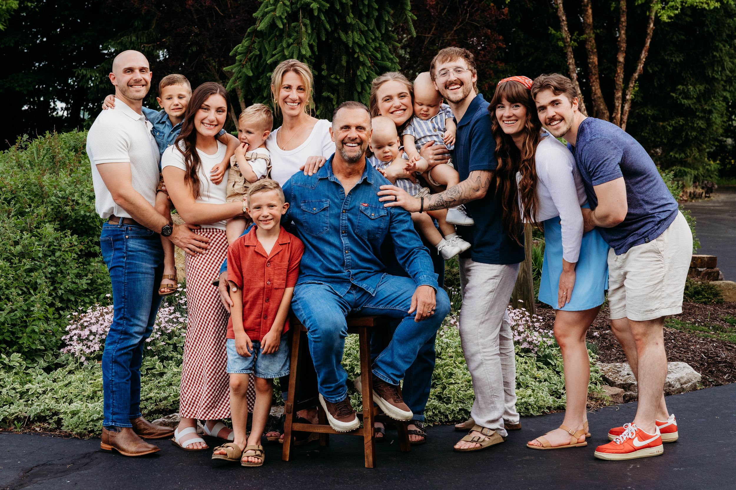 Large family group smiling together outdoors during a portrait session surrounded by lush greenery.