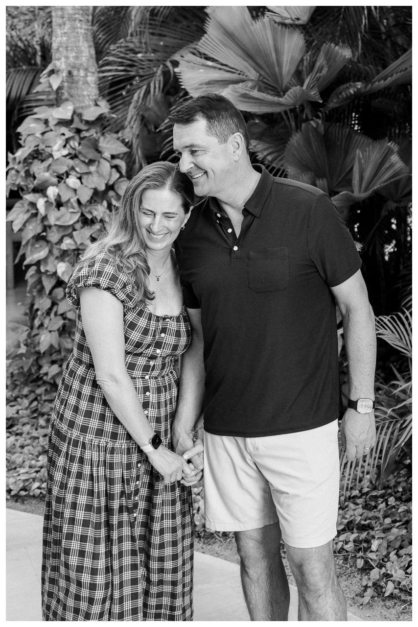Happy couple holding hands and laughing together outdoors surrounded by lush tropical greenery.