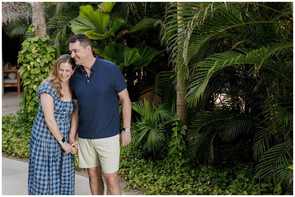 Smiling couple holding hands in a tropical garden with lush palm trees and greenery.