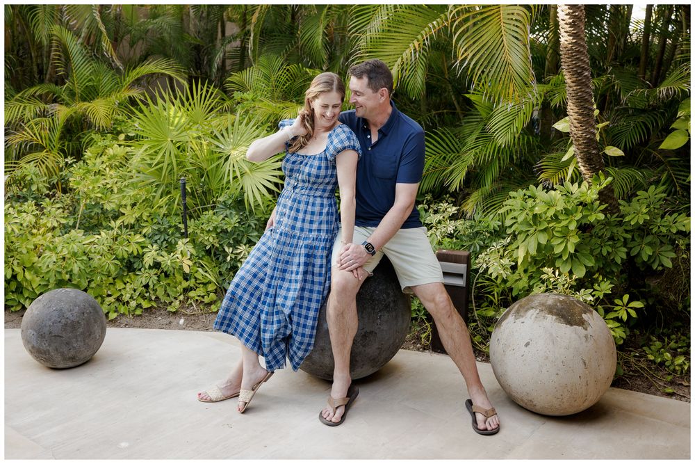 Couple posing playfully on a large stone sphere surrounded by tropical palm trees.