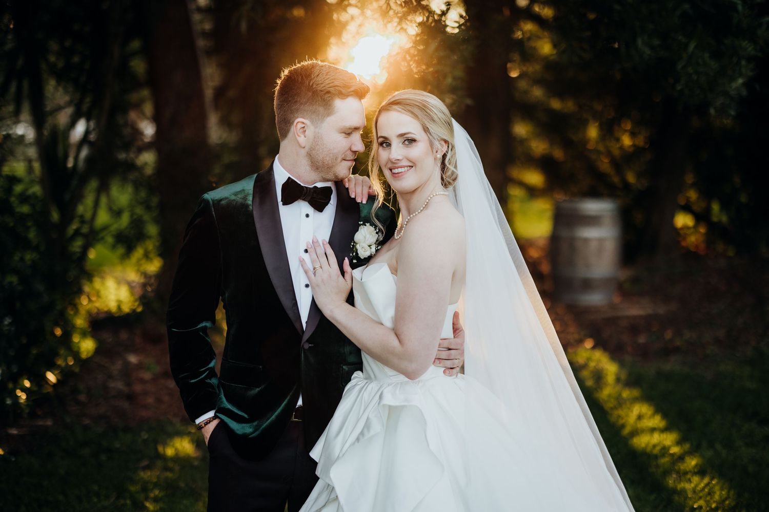Romantic sunset wedding portrait of couple embracing outdoors with golden backlighting.