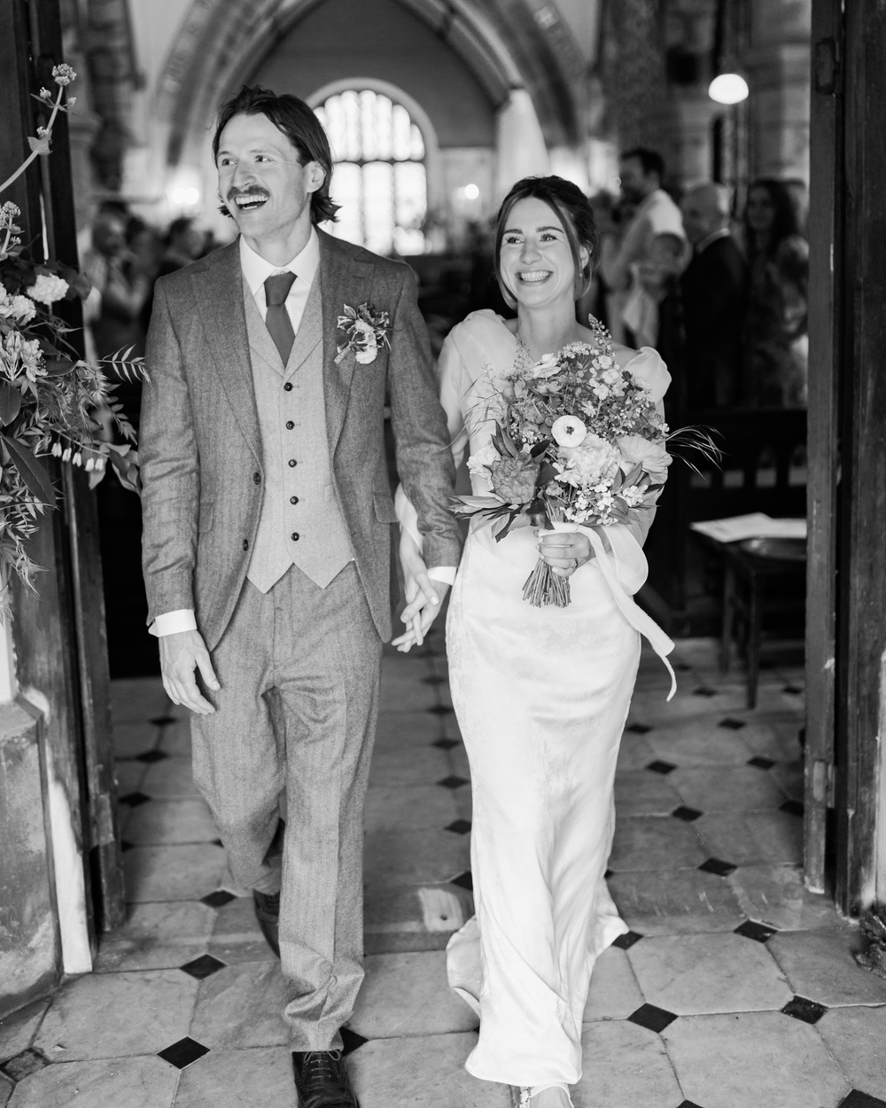 Black and white photo of a smiling bride and groom walking down the aisle after their wedding ceremony.