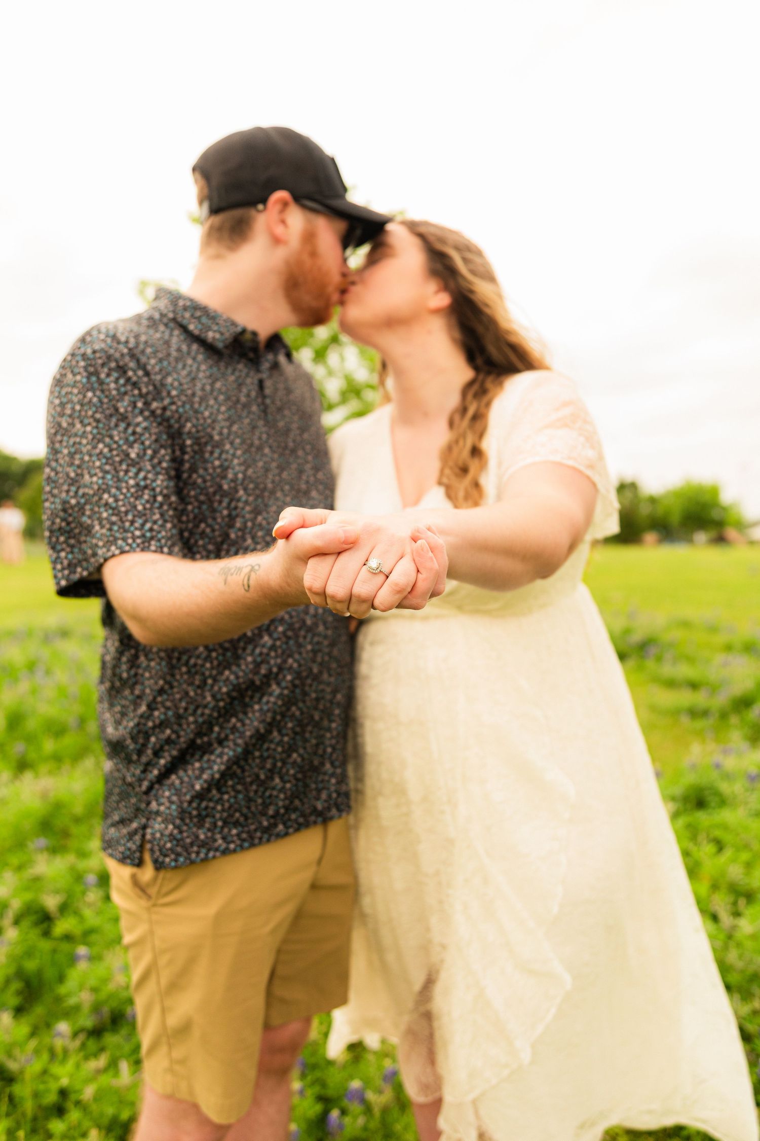 Tattooed man placing a ring on a woman's finger during a romantic outdoor proposal.