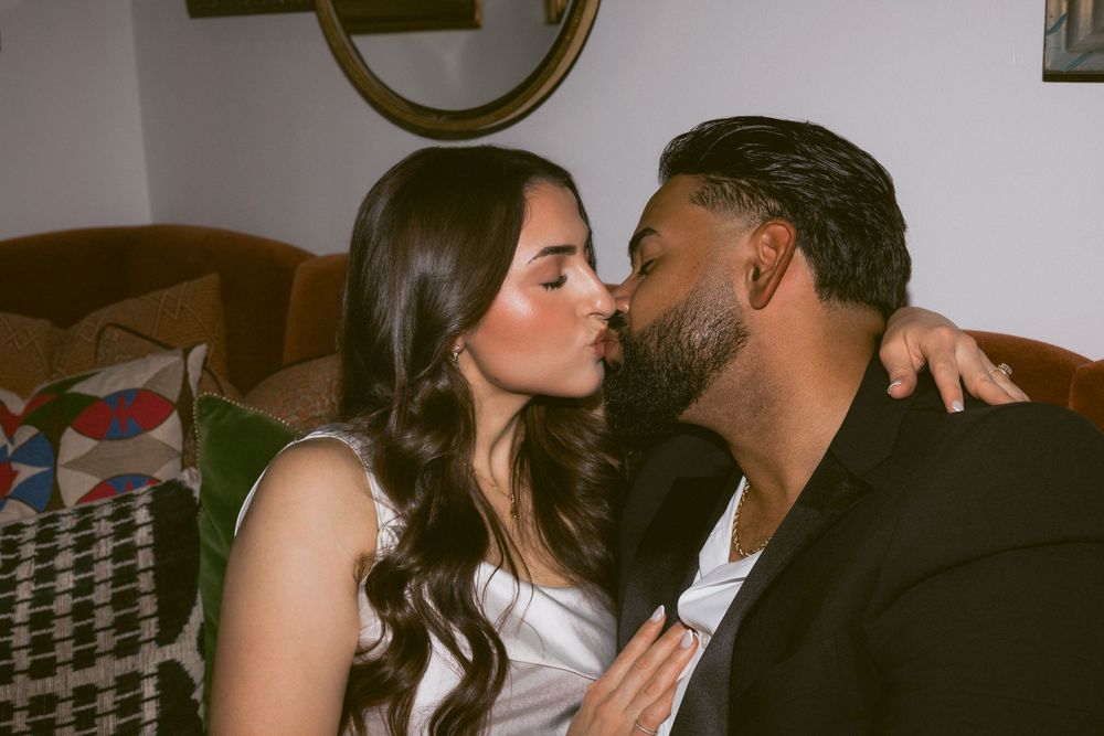 A couple sharing a romantic kiss while seated on a couch in a warmly lit indoor setting.