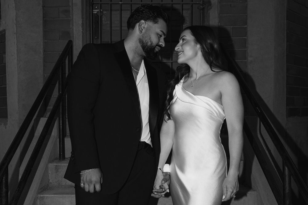 Black and white photo of a couple in formal attire smiling at each other on outdoor steps at night.