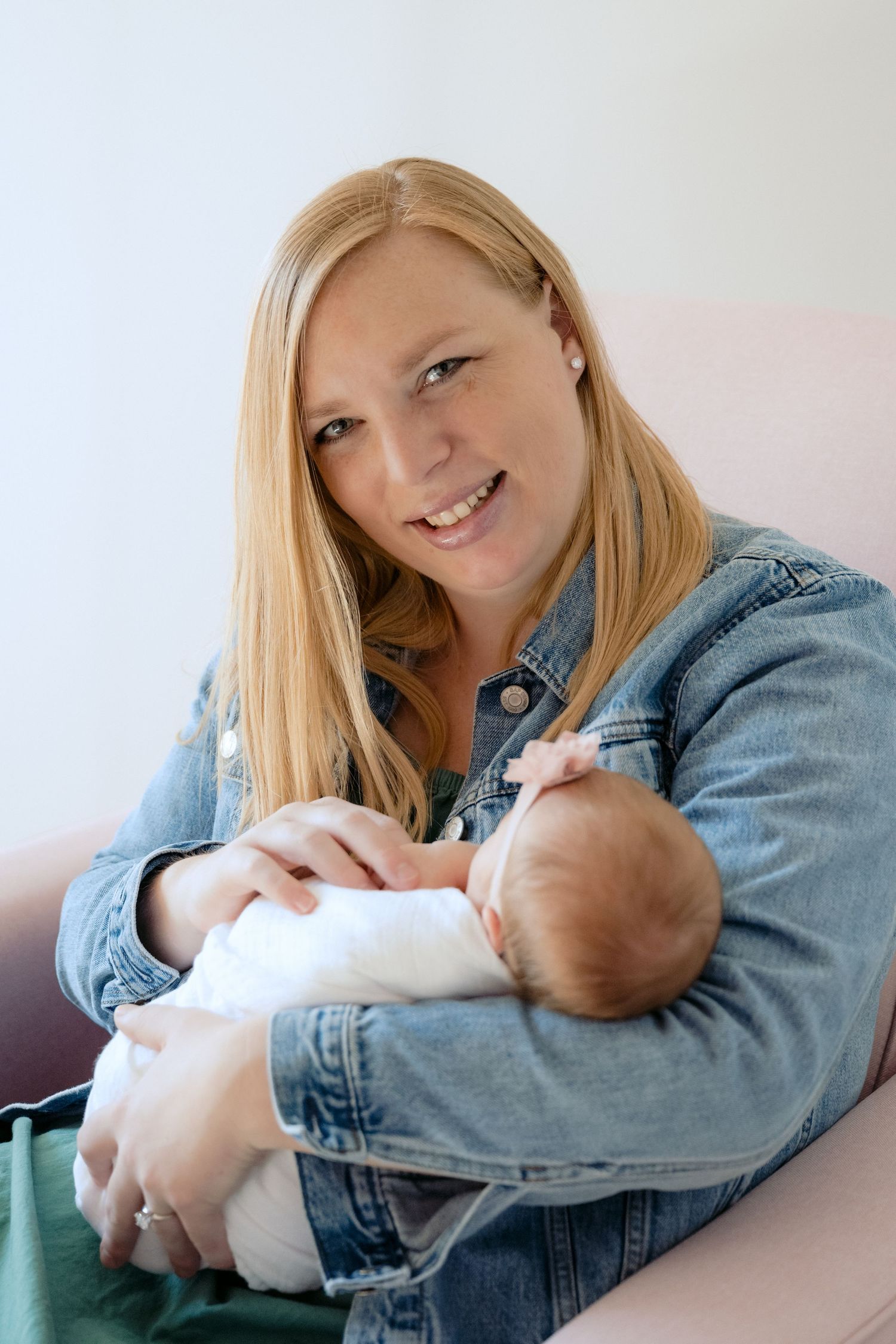 mom smiles at the camera while rocking newborn baby in nursery during in home lifestyle newborn session in lake elmo, mn