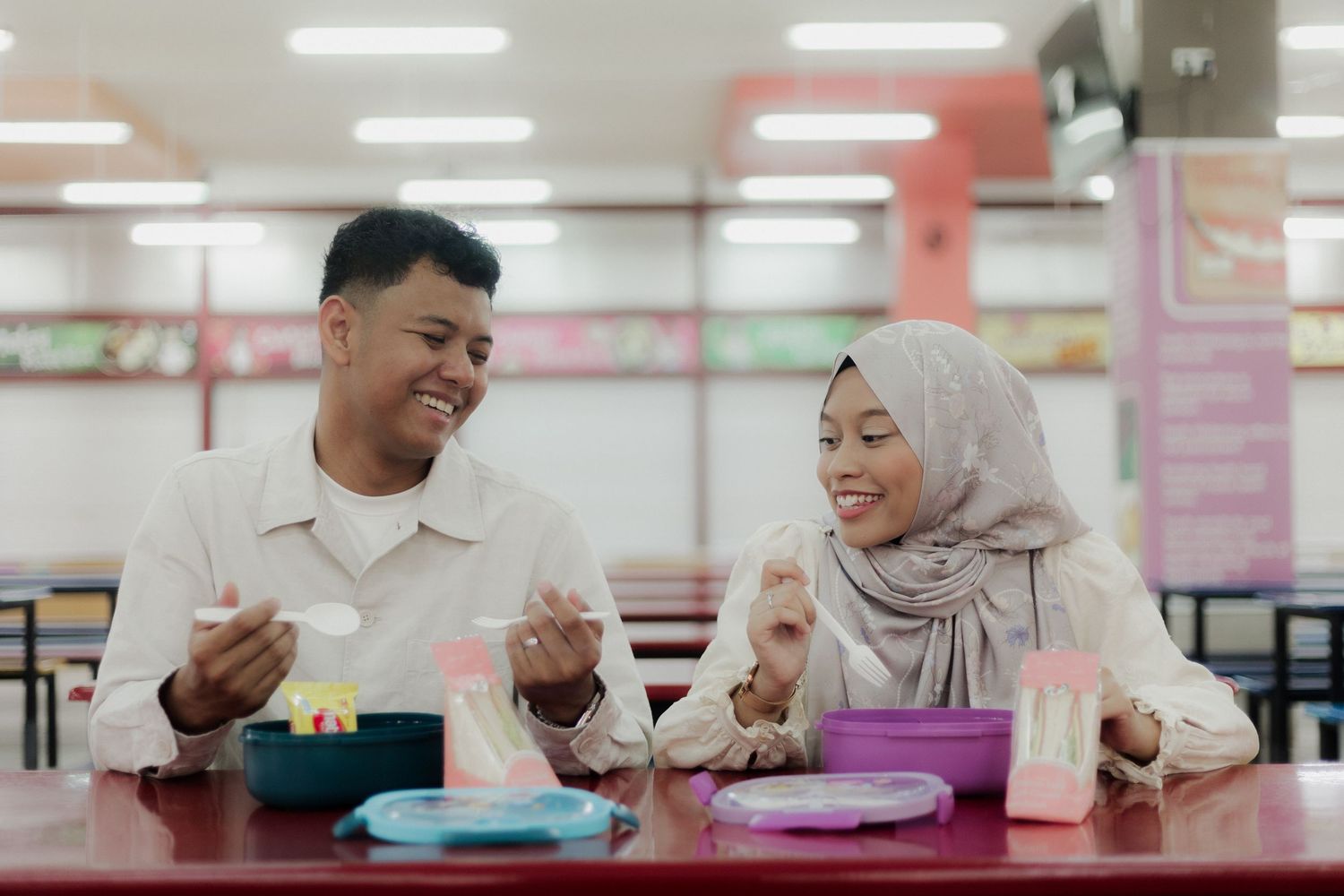 Muslim couple smiling and enjoying a meal together at a colorful fast food restaurant dining table.