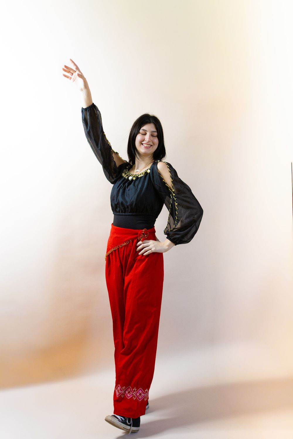 Model in red pants and black top strikes dynamic poses in studio setting.