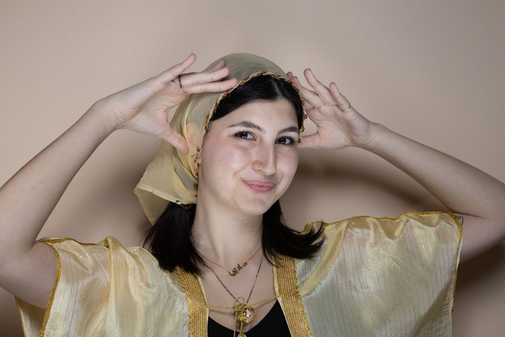 Model wearing a sheer yellow top poses against a beige background.