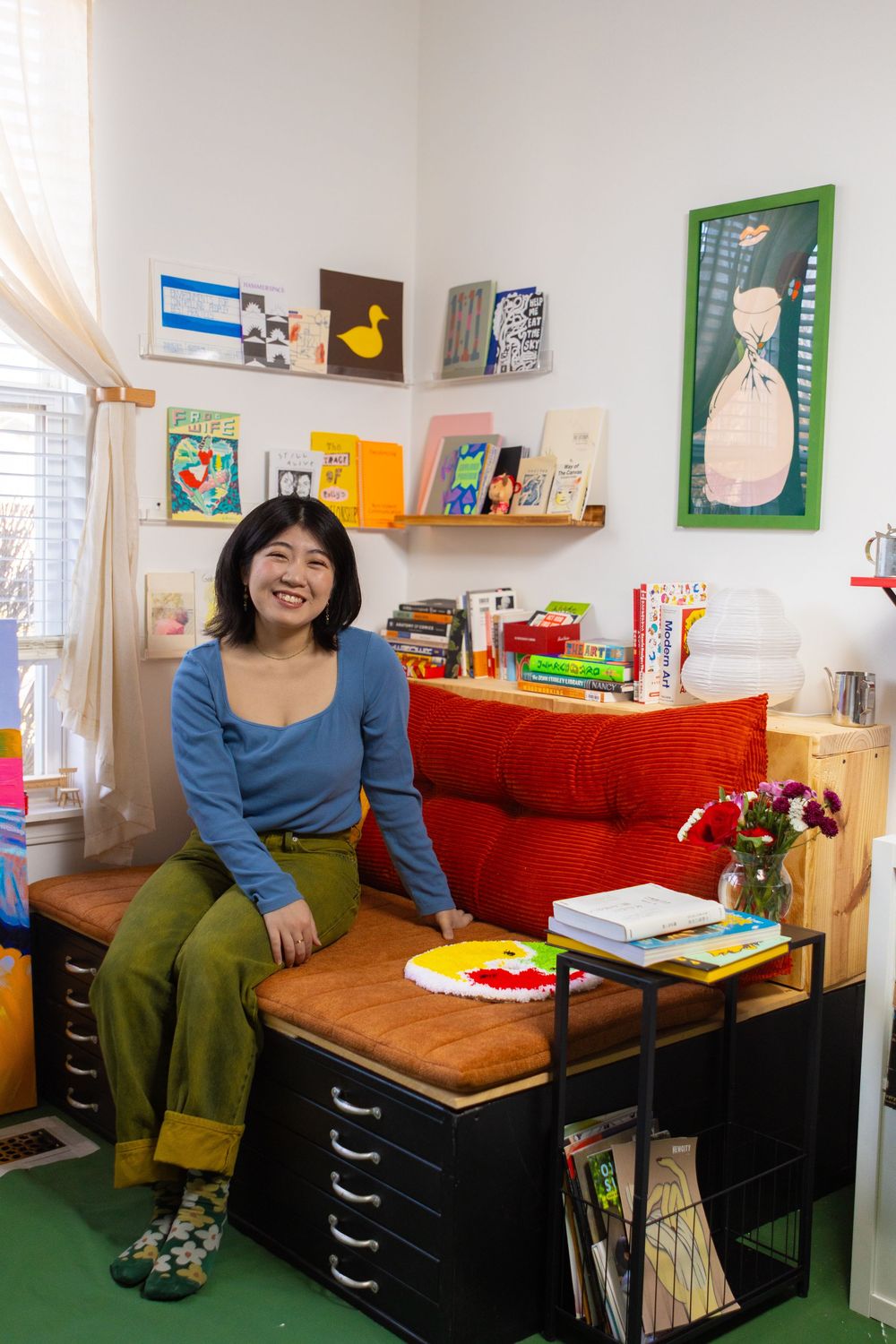 A cozy home office space with colorful artwork on walls, wooden desk, and red storage cabinet in a bright room.