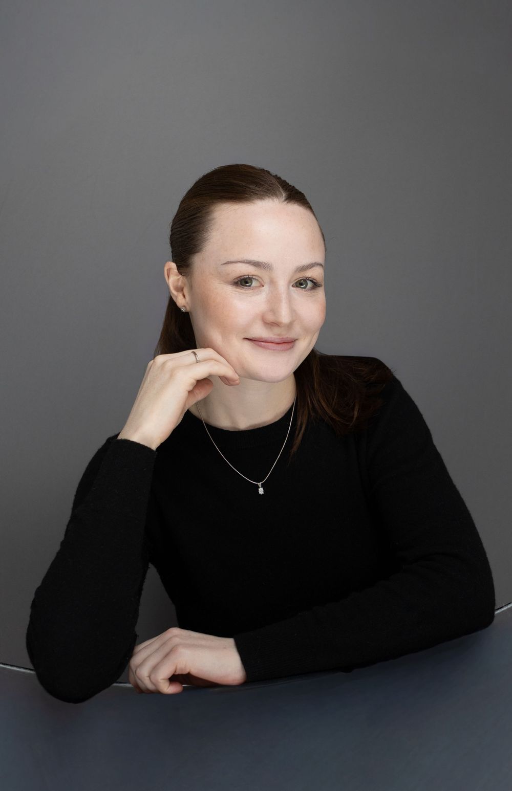 Person in black turtleneck poses for professional headshots against grey background.