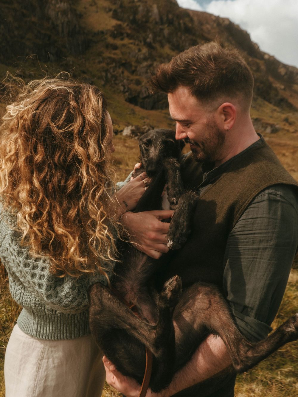 couple holding a dog inbetween them, in front of Irish landscape