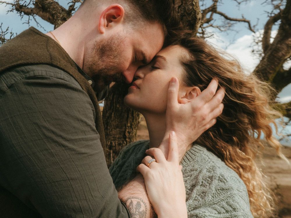 Landspace photo of couple forehead pressed against each other and him holding her face gently