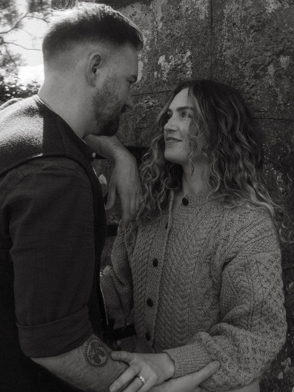 Black and white photo of a couple, she's leaning against a wall and he's gently gazing at her