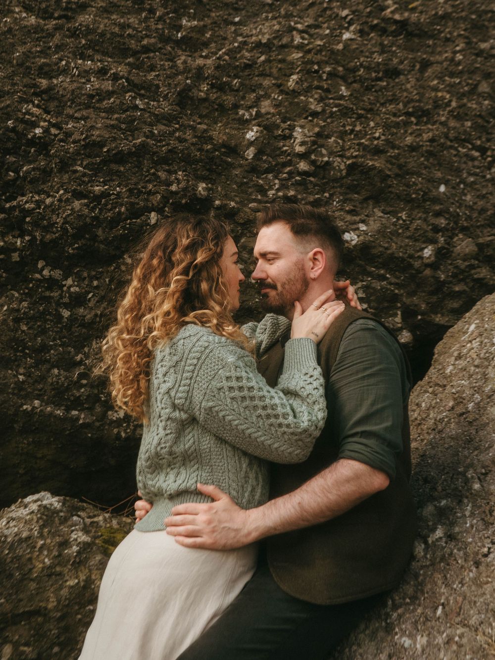 Couple facing each other leaning against rocks