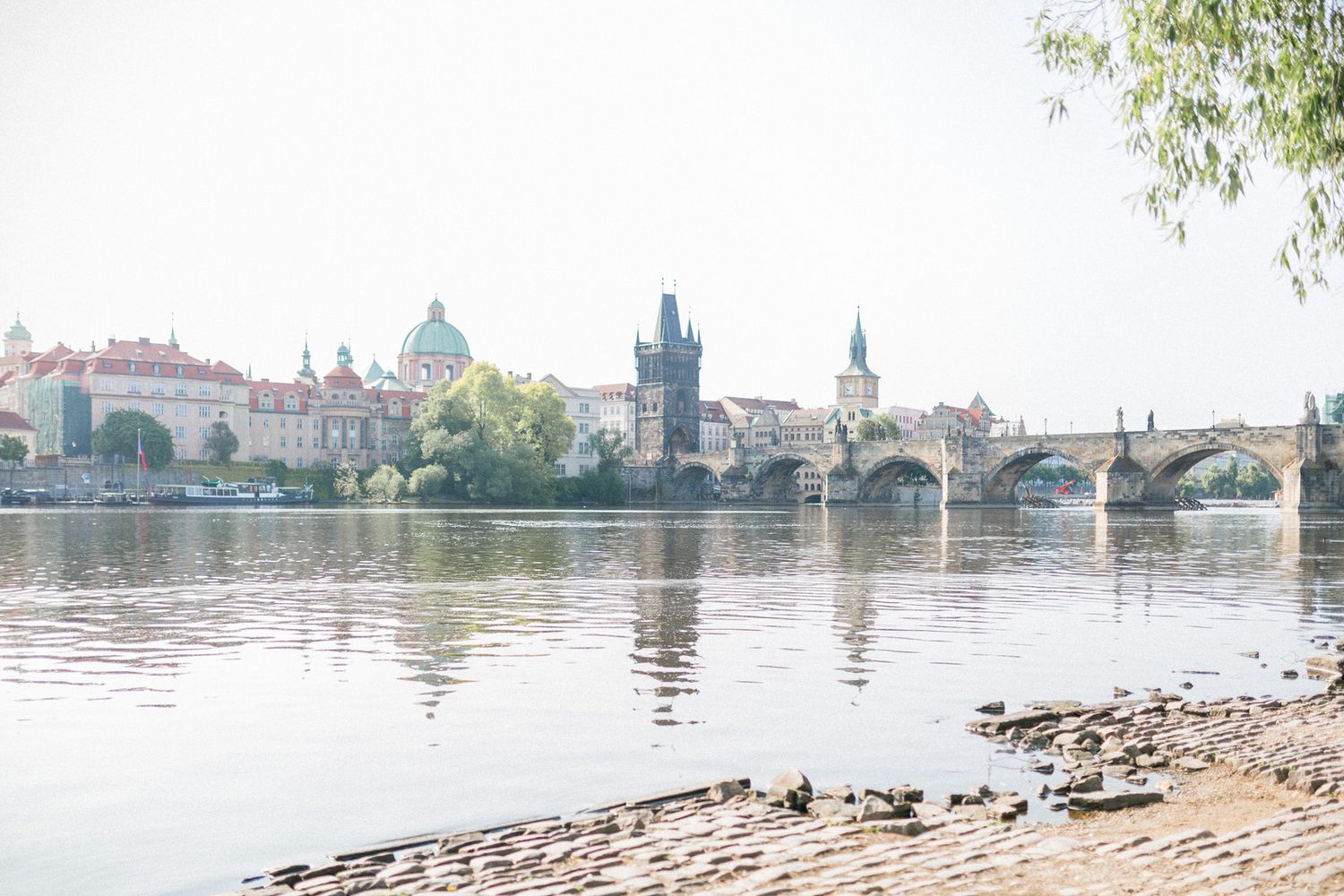 Charles Bridge and historic buildings reflect in the calm Vltava River in Prague on a peaceful morning.