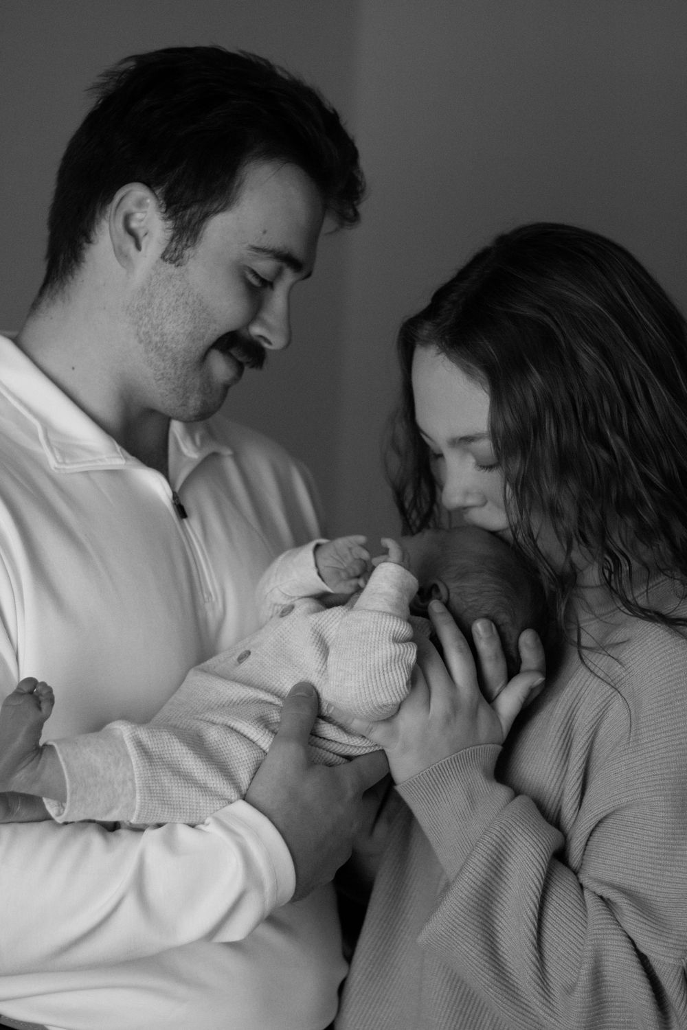 Black and white portrait of new parents lovingly holding their newborn baby together.