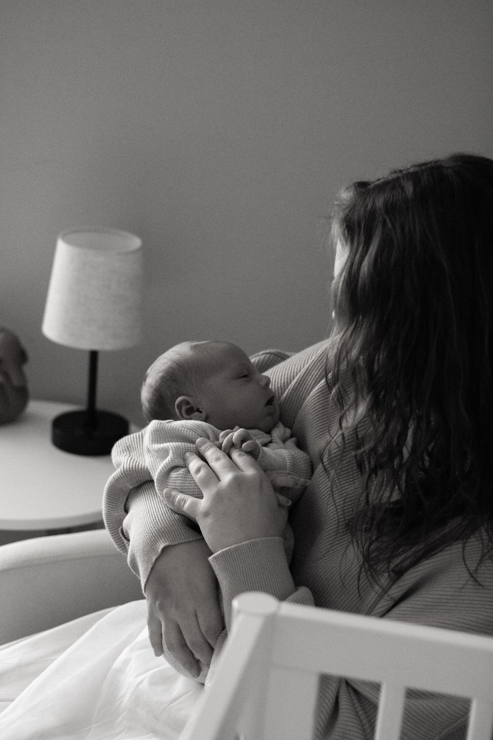 Black and white photo of a mother cradling her sleeping newborn baby near a bedside lamp.