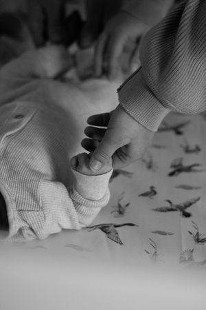 Black and white photo of an adult gently holding a newborn baby's tiny hand on a bird-print blanket.