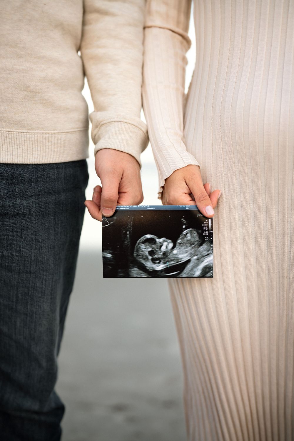 Couple holding a baby ultrasound scan together, wearing neutral tones, announcing pregnancy with sonogram photo.