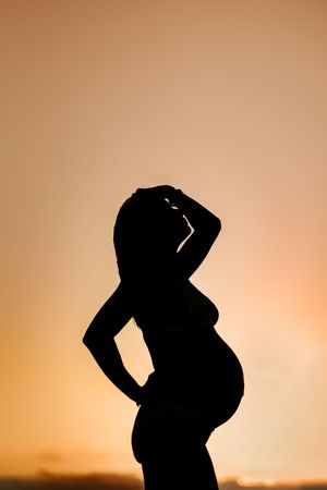 Silhouette of a pregnant woman posing against a warm golden sunset sky, highlighting her baby bump.