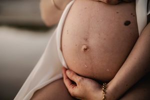 Close-up of pregnant woman's bare baby bump held gently with hands wearing gold bracelet.