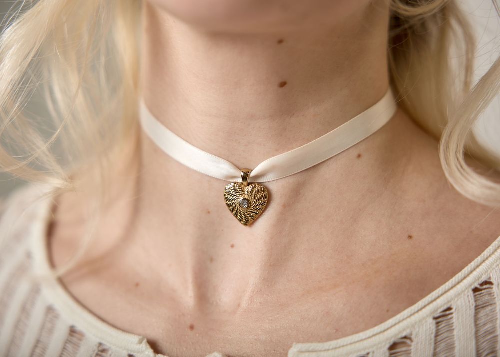 Gold ornate heart pendant choker necklace on cream ribbon worn by blonde woman.