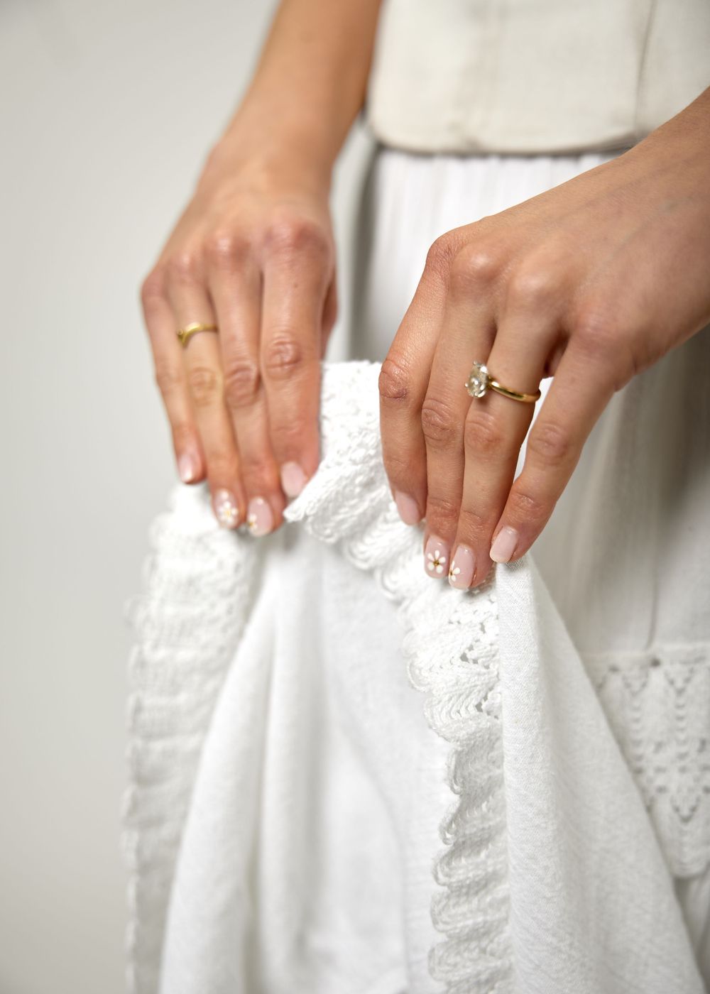 Close-up of bride's hands holding white lace wedding dress, wearing gold wedding band and diamond engagement ring.