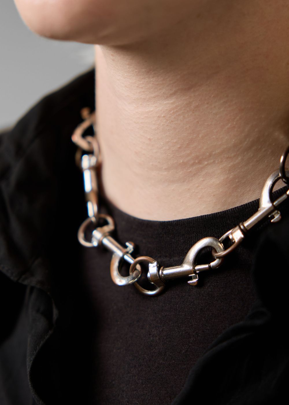 Silver chunky chain link necklace worn by a model in a black outfit, close-up neck view.