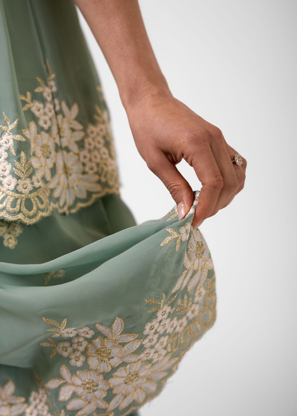 Close-up of a sage green dress with intricate gold floral embroidery and sequin details on sheer fabric.