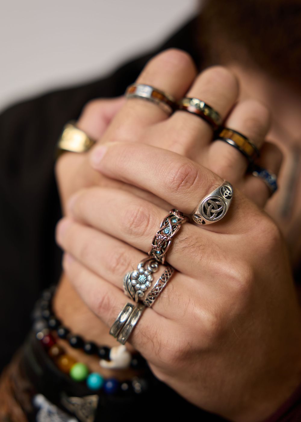 Hands adorned with multiple silver rings and colorful beaded bracelets clasped together.