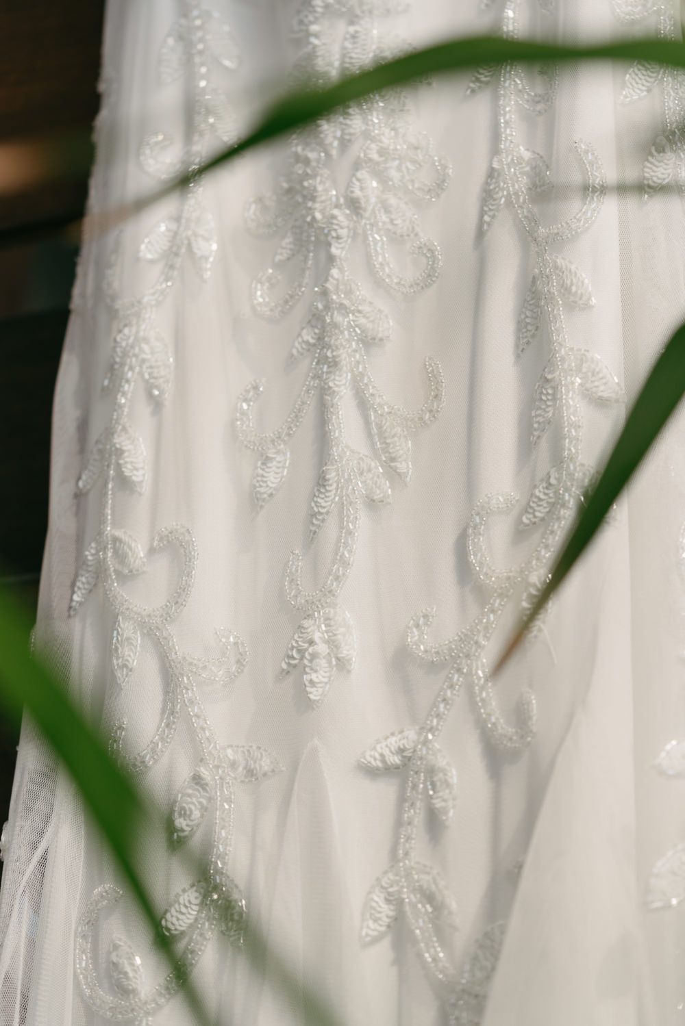 Close-up of an elegant white wedding dress featuring intricate beaded lace embroidery with floral and scroll patterns.