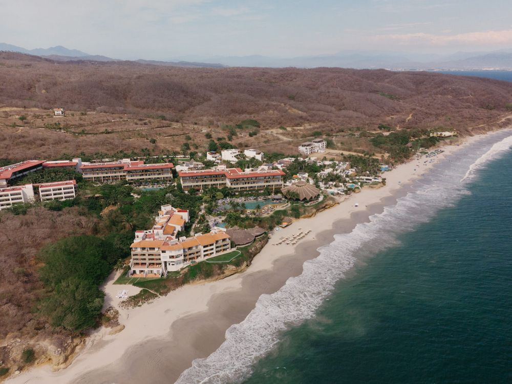 Aerial view of a beachfront resort nestled between mountains and Pacific Ocean coastline in Mexico.