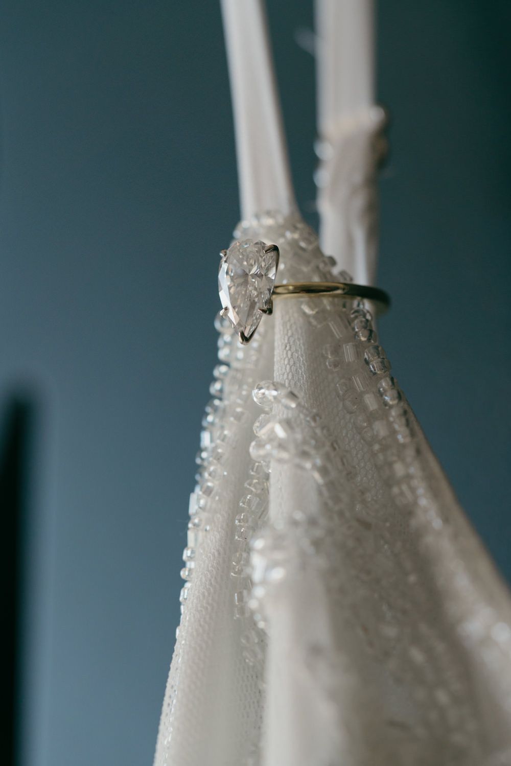 Close-up of a diamond engagement ring placed on a wet white wedding dress with water droplets.