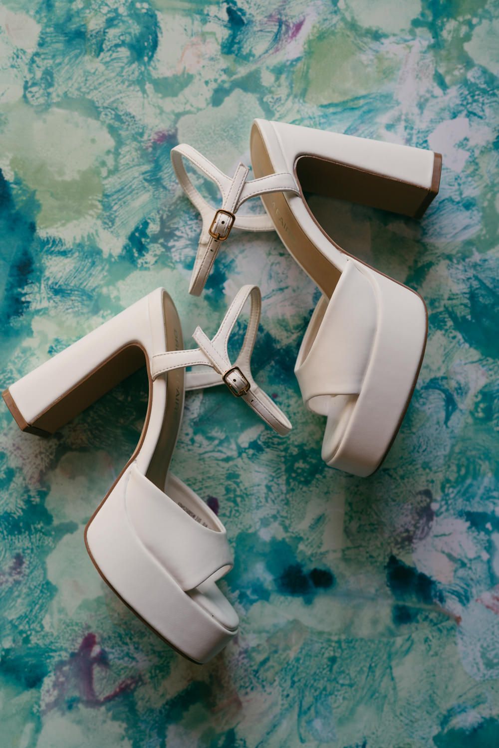 White leather platform block heel bridal sandals with ankle straps on a watercolor background.