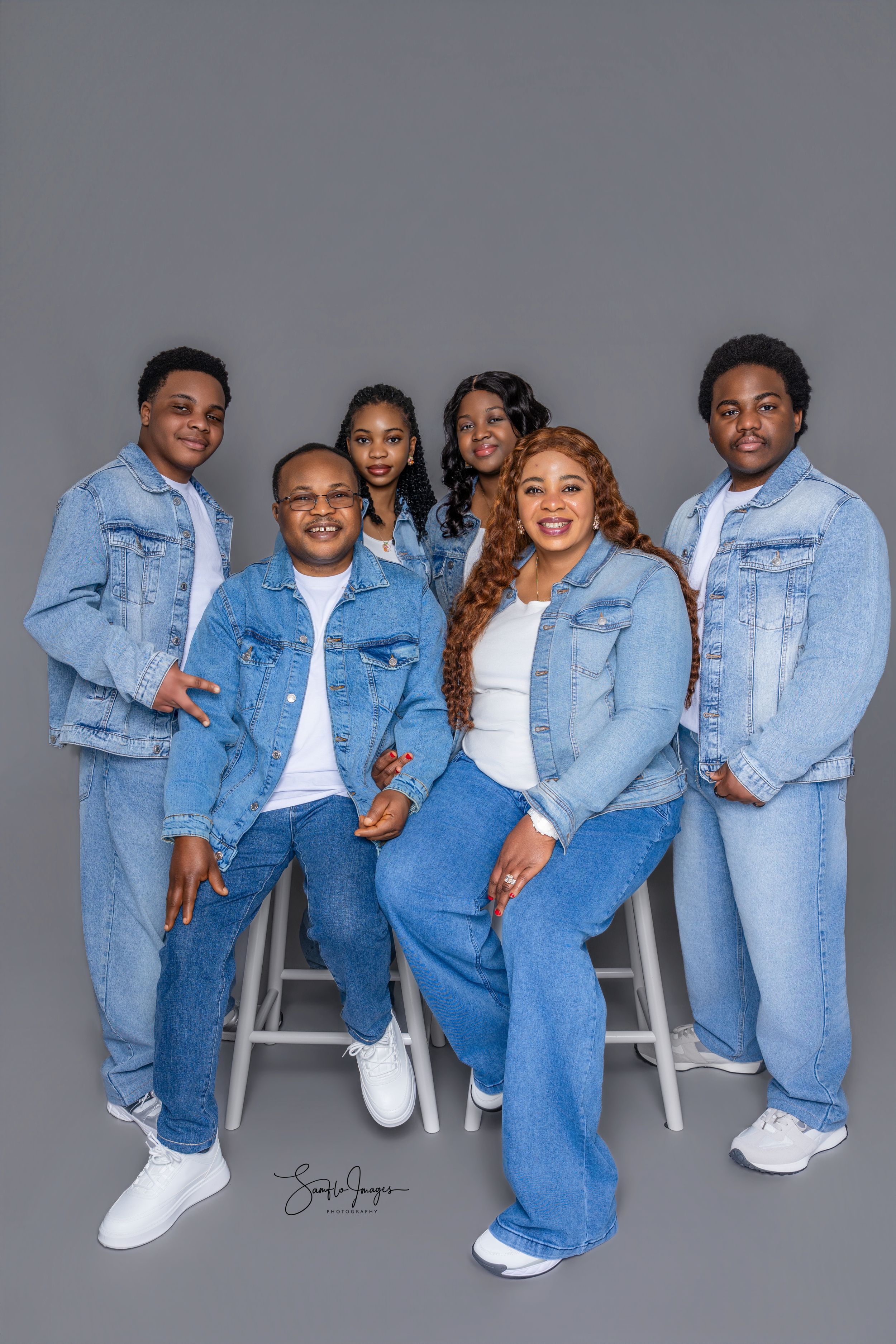 A family of six poses together in matching denim outfits against a gray studio backdrop.