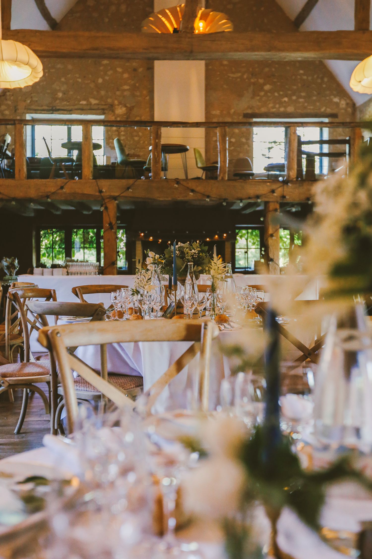 Elegant barn wedding reception with rustic wooden chairs, floral centerpieces, and string lights in a stone venue.