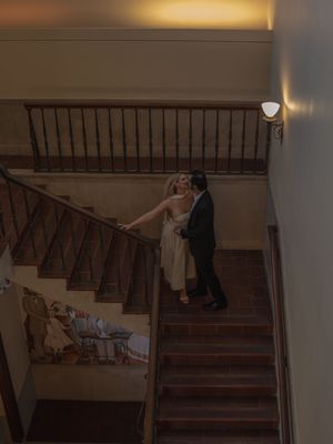 Wedding couple sharing a tender embrace on a wooden staircase with decorative mural in background.