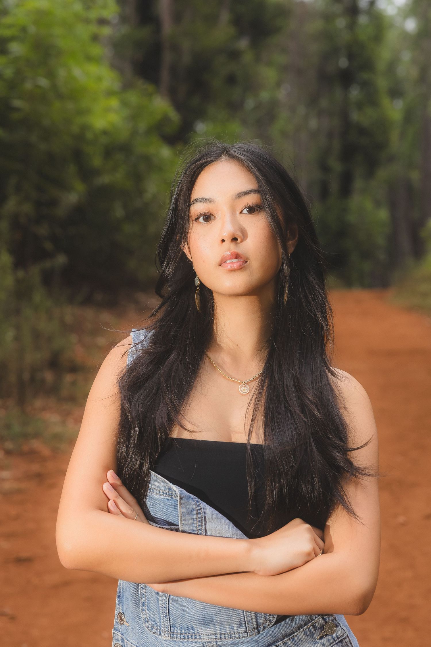 Young Asian woman with long black hair posing on a red dirt forest path.