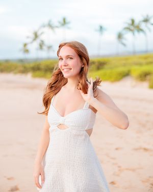 Young woman in white dress smiling on a tropical beach with palm trees.