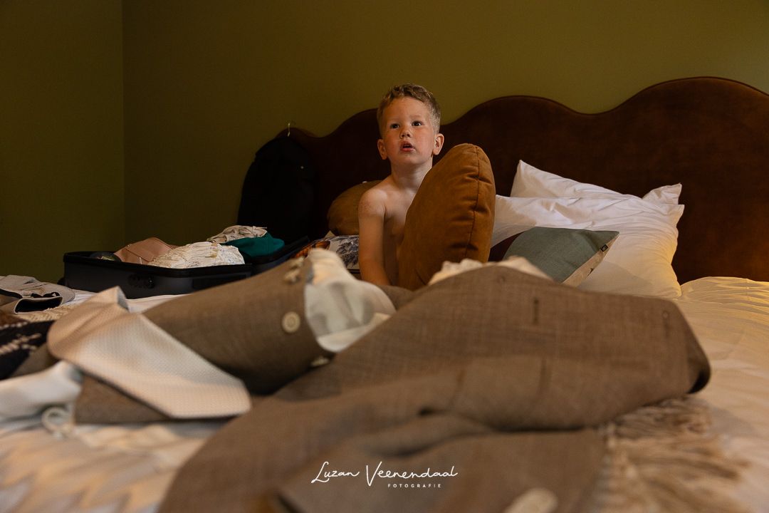 Zoontje Finn zit met tussen de kleding op het bed klaar om zich aan te kleden getting ready bruiloft Jesse en Sharon, Zoomers Castricum