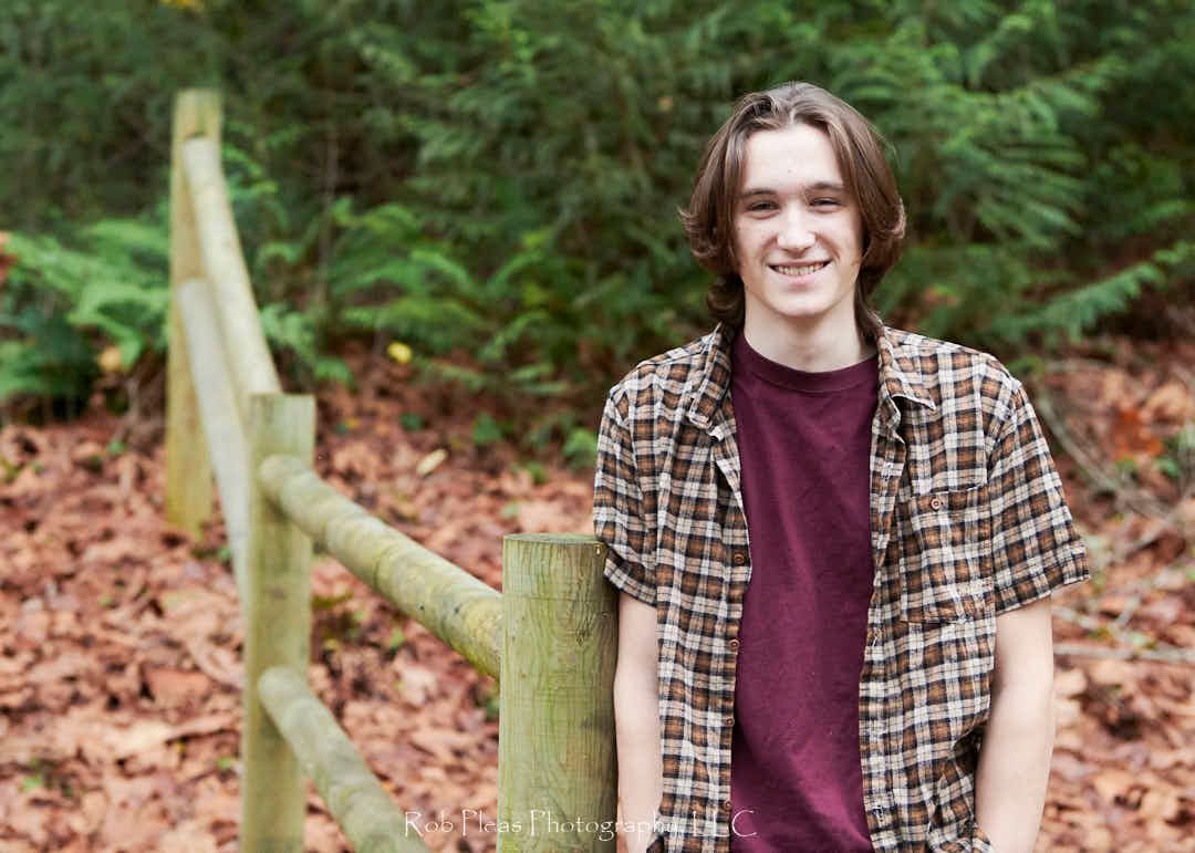 High school senior male smiling, while leaning against fence at Snoqualmie-Preston trailhead.