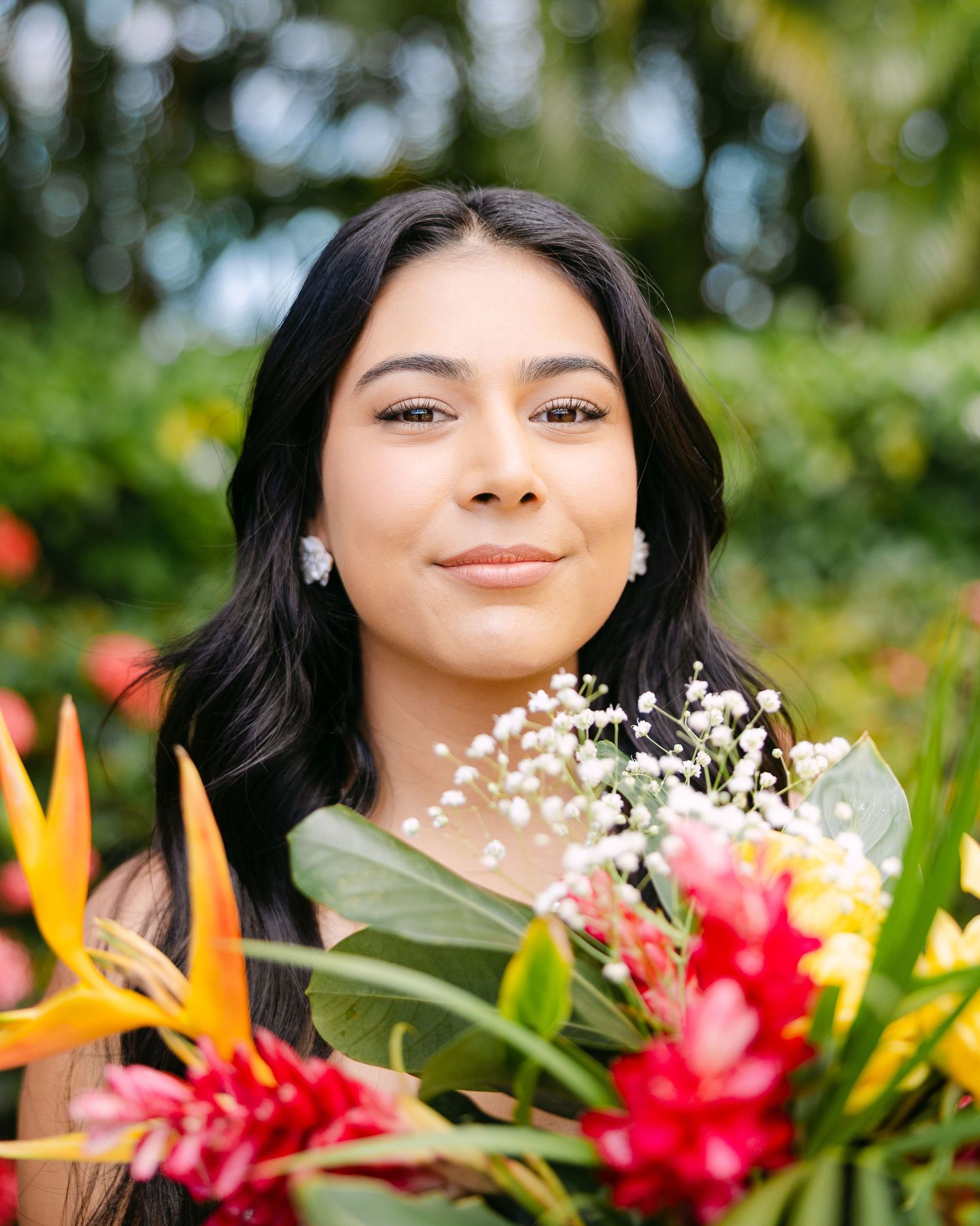 A young woman smiles holding a vibrant tropical bouquet of birds of paradise and red flowers.