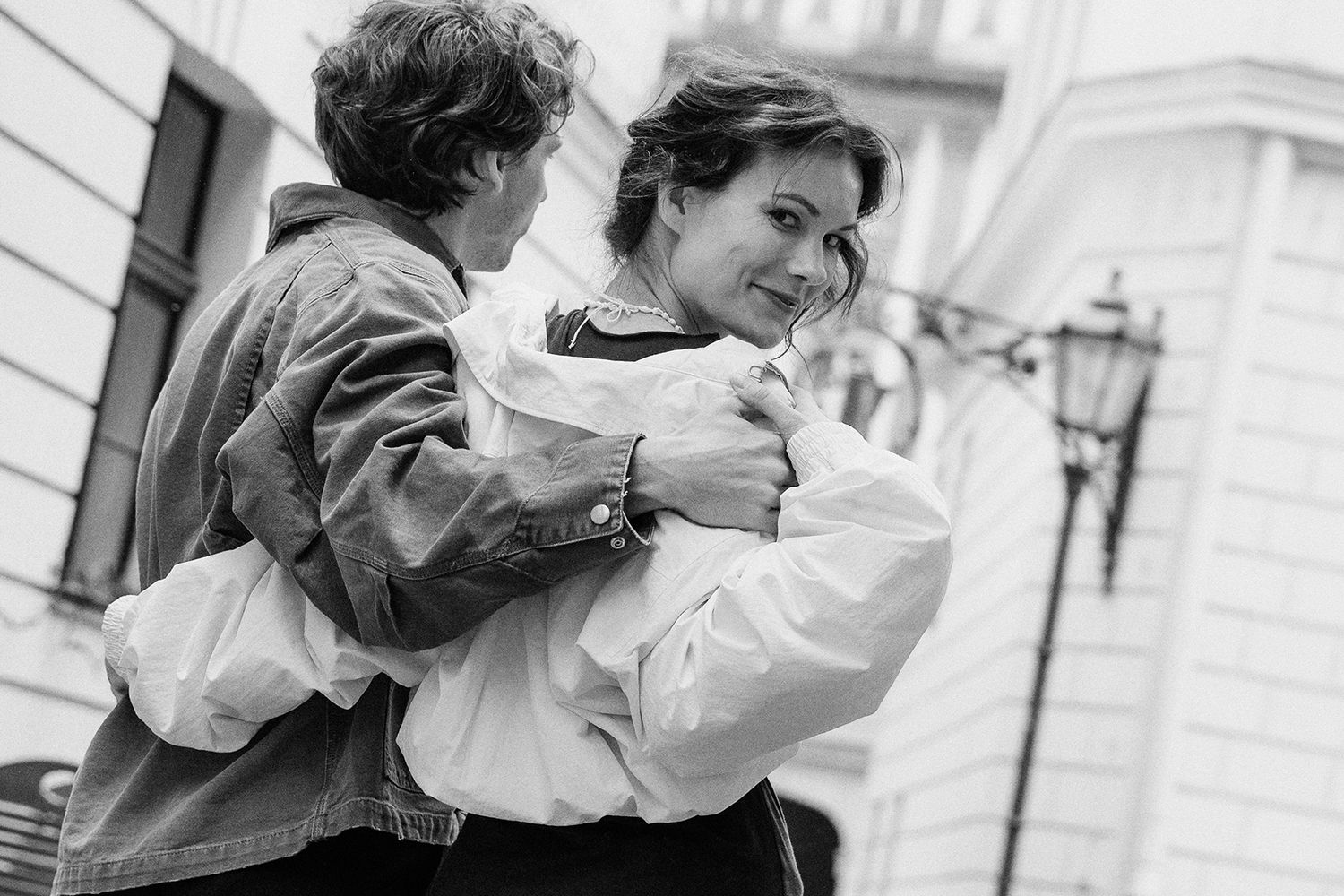Black and white photo of a couple embracing and smiling outdoors walking down the street.