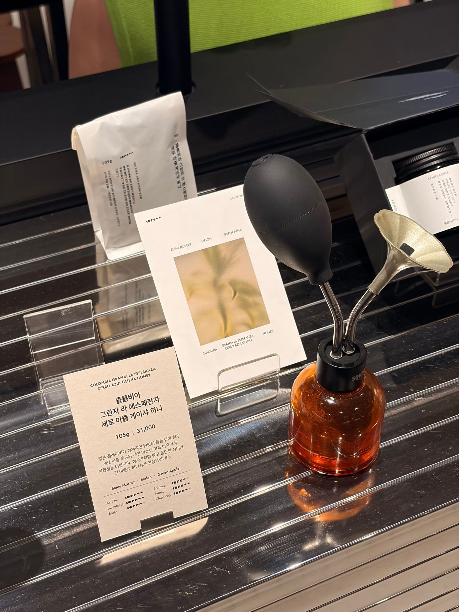 Amber glass bottle with black funnel diffuser beside Korean coffee packaging cards on a display shelf.