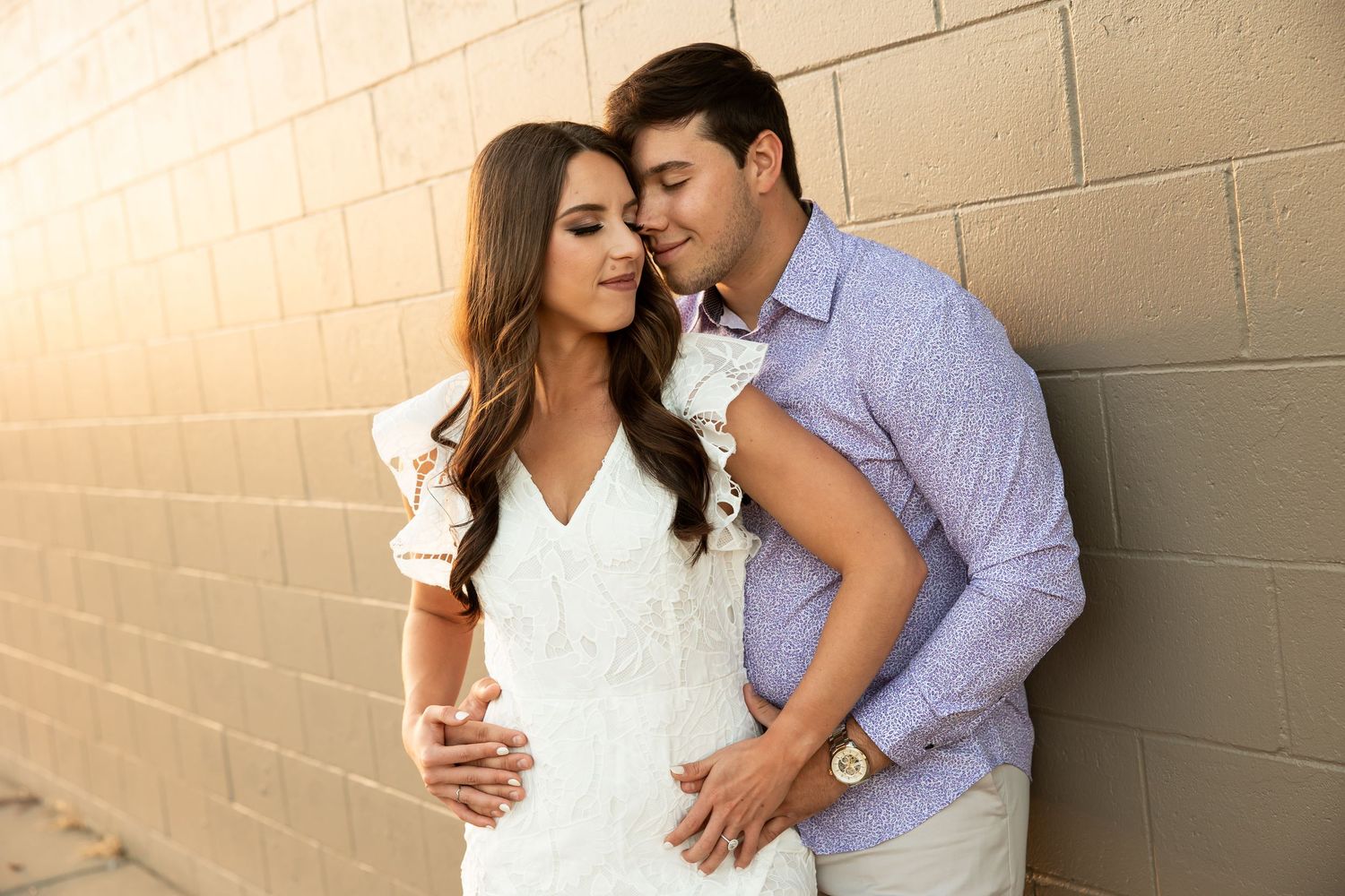 Couple sharing a romantic moment leaning against a brick wall at golden hour.