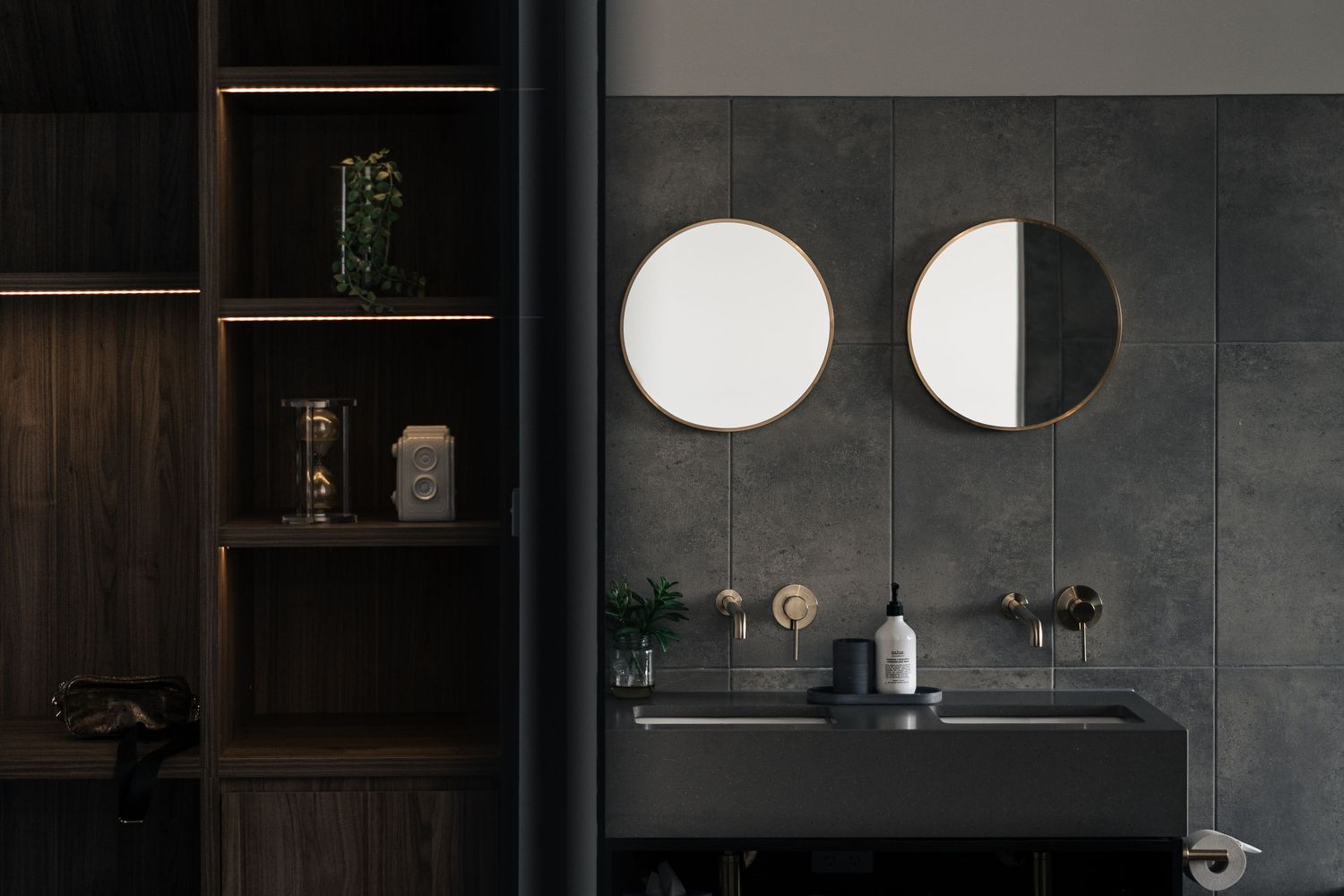 Sophisticated dark bathroom with twin round gold-framed mirrors, black wall-mounted vanity, and illuminated open shelving unit.

Lux on Max